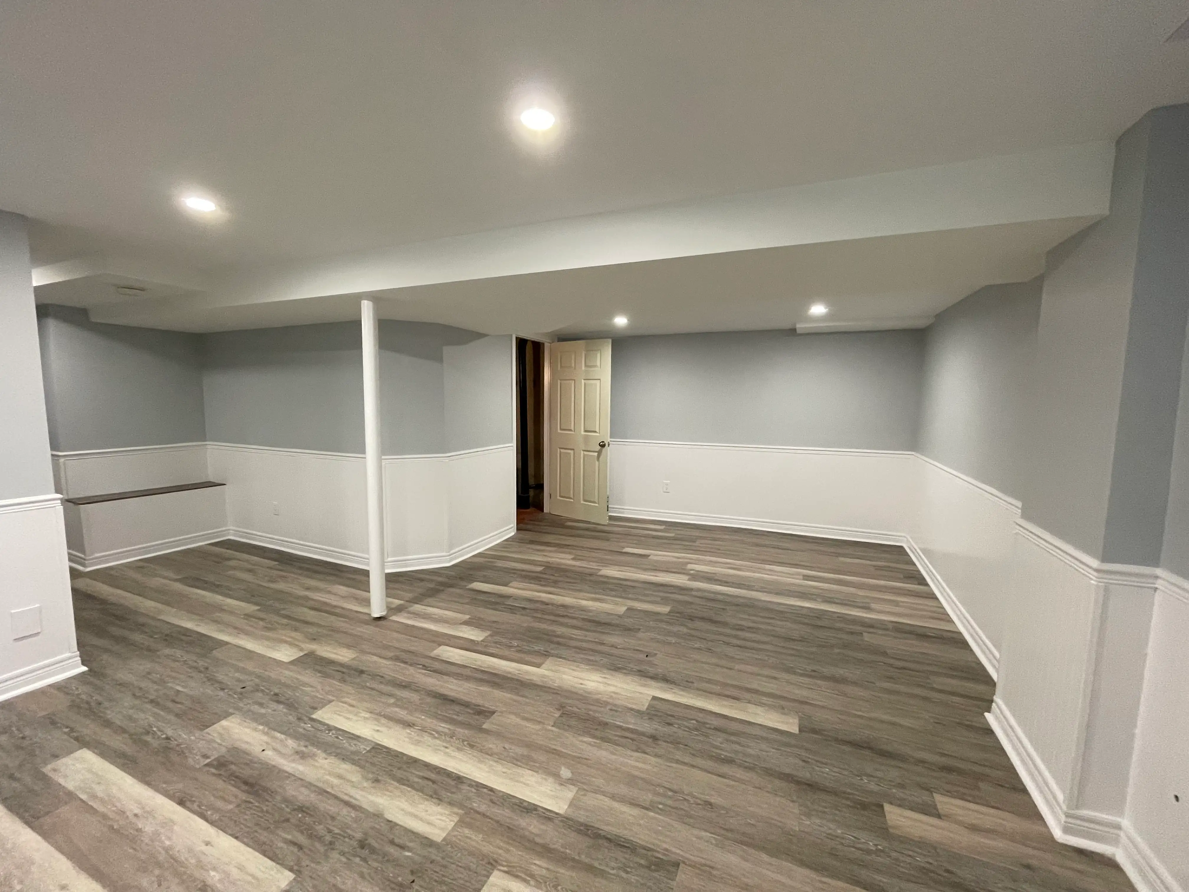 Bright finished basement by HMH Construction with grey vinyl plank flooring, wainscoting and pot lights