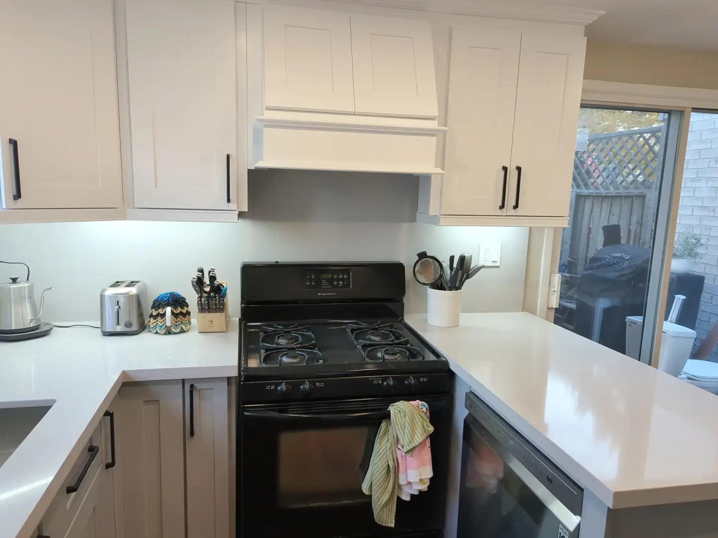 The same wall after renovation — shaker cabinets, custom hood surround and quartz counters