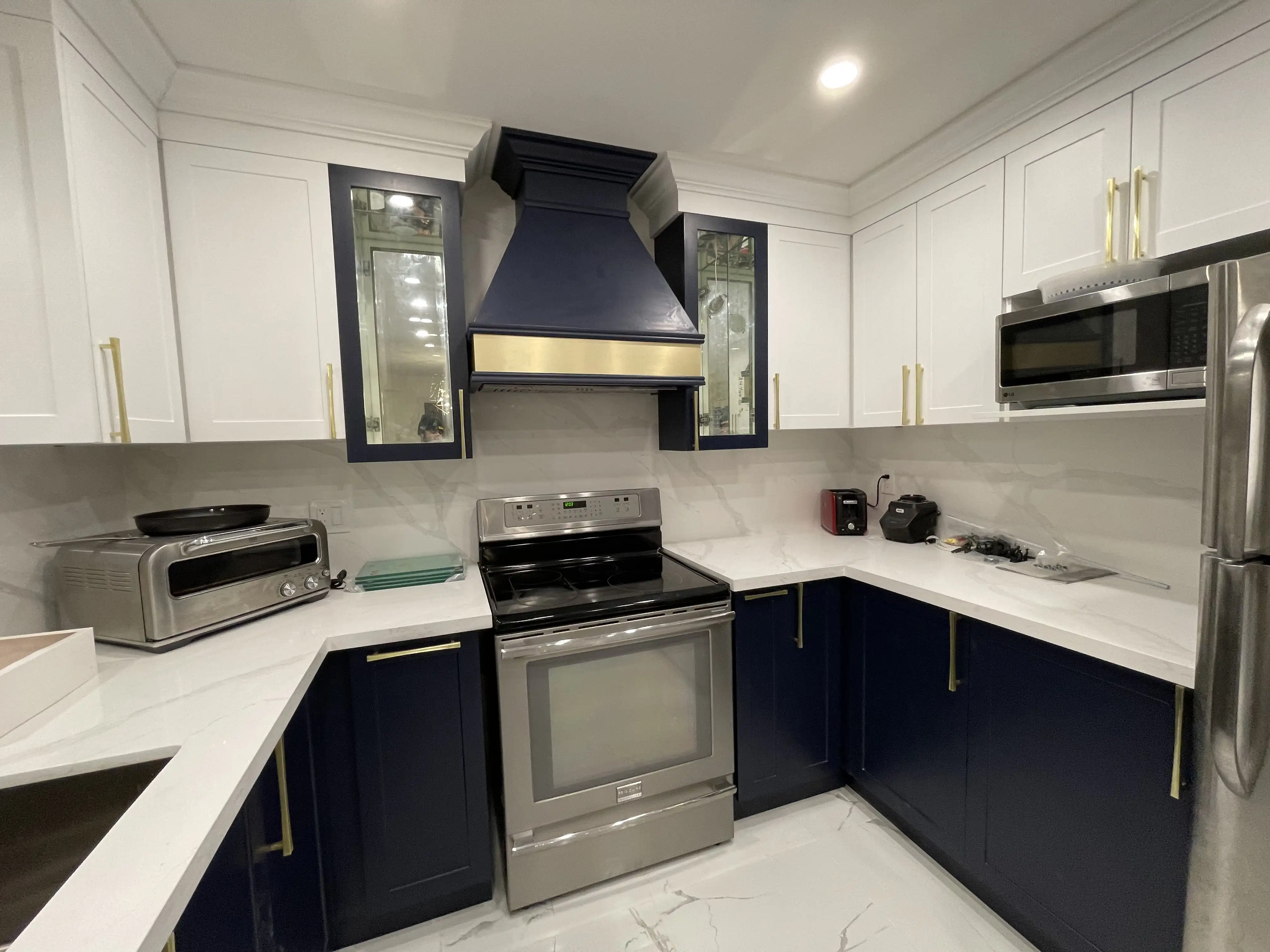 Renovated two-tone kitchen by HMH Construction with navy lower cabinets, brass hardware and quartz counters